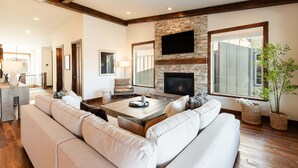 A living room with a fireplace, a large sofa, a coffee table, and a television mounted on the wall. - Mayflower Vista - Deer Valley East Basecamp for All Seassons w/ Views, Private Hot Tub (Heber City)