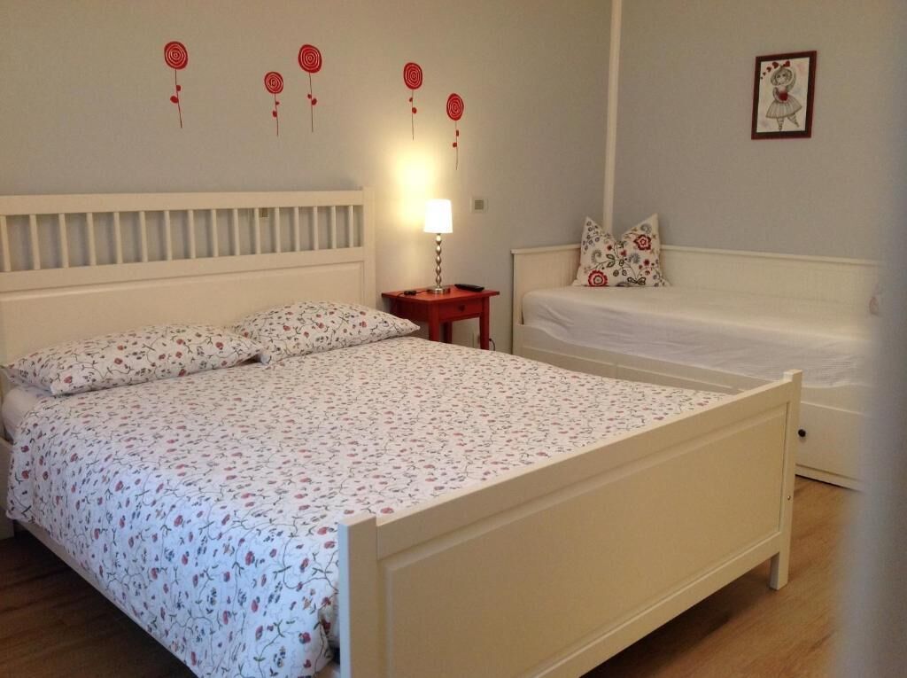 Un dormitorio con una cama grande, una cama más pequeña, una mesita de noche con lámpara y una pared decorada.