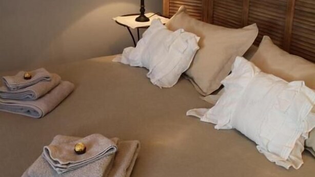 Un lit bien fait, avec une literie et des oreillers de couleur beige, une lampe de chevet et une fenêtre avec des rideaux.