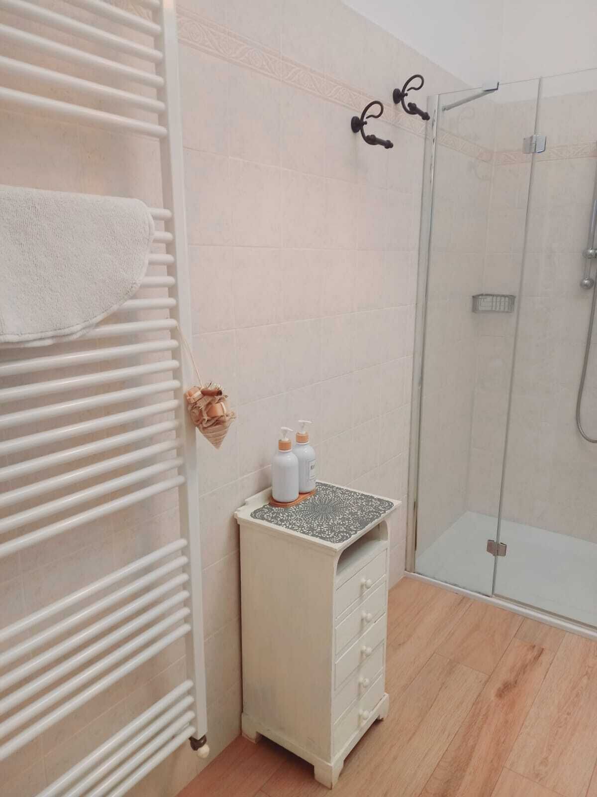 Un baño con toallero blanco, tocador pequeño con bandeja estampada y cabina de ducha de vidrio.