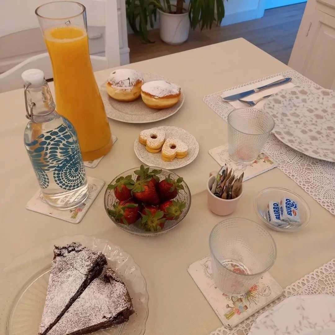 Et morgenbord med et glas appelsinjuice, en vandflaske, en tallerken med donuts, en skål jordbær, et stykke kage og en kop kaffe.