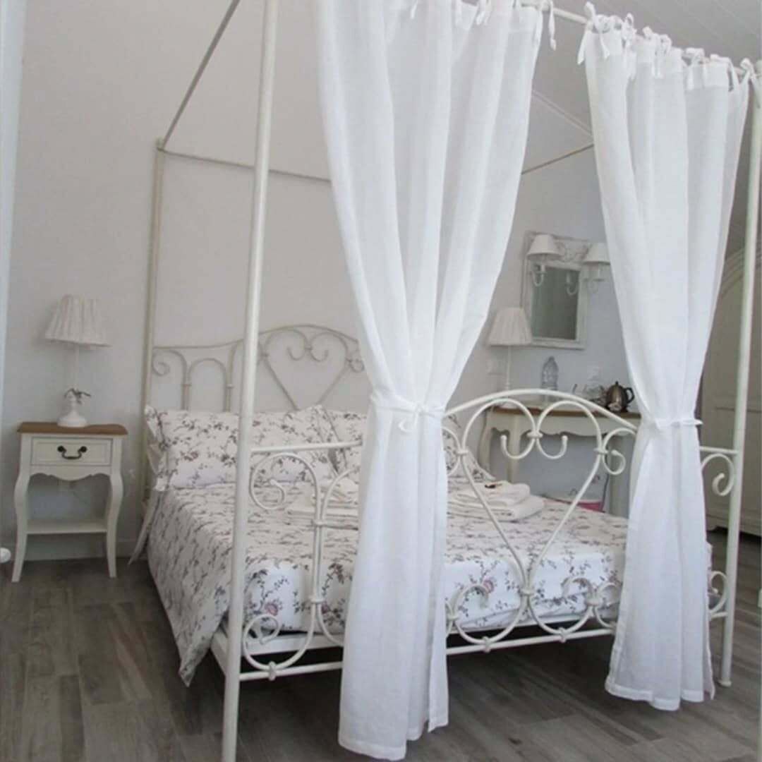 A four-poster canopy bed with a floral bedspread, a bedside table with a lamp, and a nightstand.