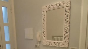 Une pièce comprenant une console blanche, un miroir décoratif doté d’un cadre orné et un petit récipient en verre posé sur la console.