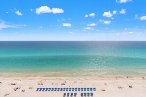 A beach with clear blue water, a sandy shore, and a row of blue umbrellas. - Seas the Day! Your Perfect 2BR Beachfront Escape! Sleeps 8! (Panama City Beach)