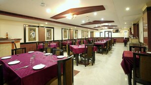 A banquet hall with multiple tables covered in red tablecloths, arranged in rows. - WORMWOOD SYNERGY SRIYASH REGENCY (Bhagalpur)