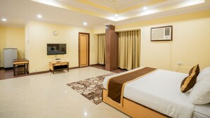 A hotel room with a bed, a TV, a desk, a wardrobe, and a ceiling fan. - WORMWOOD SYNERGY SRIYASH REGENCY (Bhagalpur)