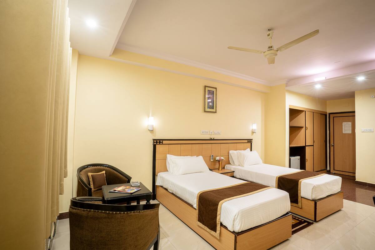 A hotel room with two beds, a desk, a chair, and a wardrobe.