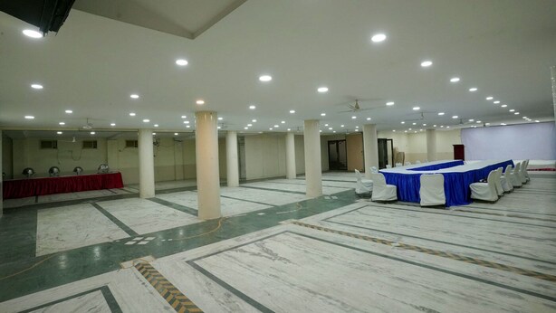 A large, well-lit hall with a marble floor, multiple tables with blue and white tablecloths, and white chairs arranged for events. - WORMWOOD SYNERGY SRIYASH REGENCY (Bhagalpur)