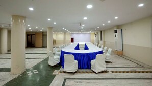 A conference room with a long table, white chairs, and a ceiling fan. - WORMWOOD SYNERGY SRIYASH REGENCY (Bhagalpur)
