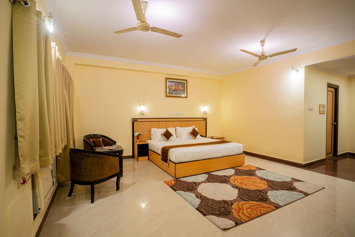 A hotel room with a bed, a chair, a nightstand, a ceiling fan, and a carpet.