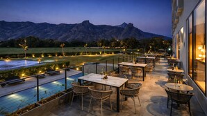 An outdoor terrace with tables and chairs, a pool, and a mountain view. - Avisa Hotel & Resort Abu Road - Luxury Pool & Mountain View (Abu Road)