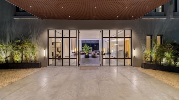 A modern hotel lobby with a wooden ceiling, glass doors leading to a seating area, and potted plants. - Avisa Hotel & Resort Abu Road - Luxury Pool & Mountain View (Abu Road)
