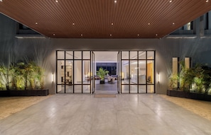 Eine moderne Hotelhalle mit Holzboden, Glastüren zu einer Lounge und Zimmerpflanzen.