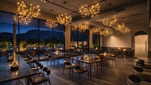 An indoor dining area with tables and chairs, large windows, and hanging light fixtures. - Avisa Hotel & Resort Abu Road - Luxury Pool & Mountain View (Abu Road)