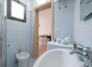Ein Badezimmer mit Badewanne, Waschbecken und Bidet. Über dem Waschbecken befindet sich ein Fenster und eine Tür führt in einen Essbereich.