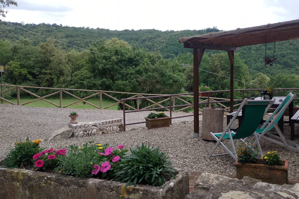 Een overdekt terras met stoelen en tafels, omgeven door grind en potplanten.