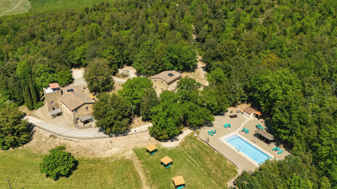 An aerial view of a property with multiple buildings, a swimming pool, and surrounding greenery.