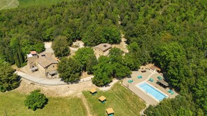 Vista aérea de uma propriedade com vários edifícios, piscina e vegetação ao redor.