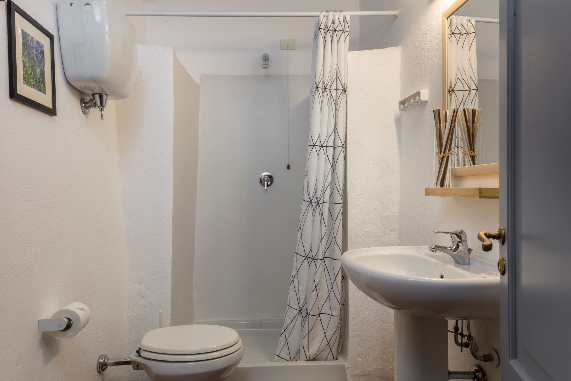 A bathroom with a toilet, sink, shower, and a framed picture on the wall.