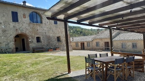 Um edifício rústico de pedra com um alpendre coberto, com mesas e cadeiras de madeira.