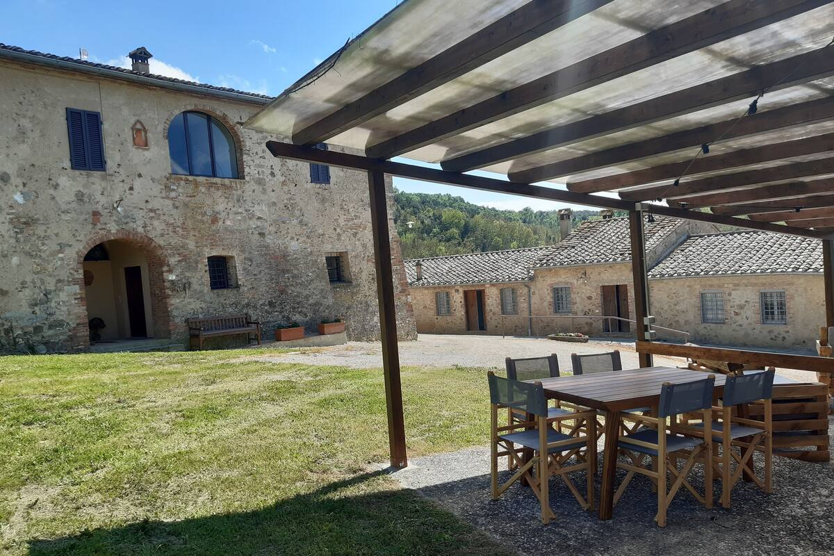 Een landelijk stenen gebouw met een overdekte patio, voorzien van houten tafels en stoelen.