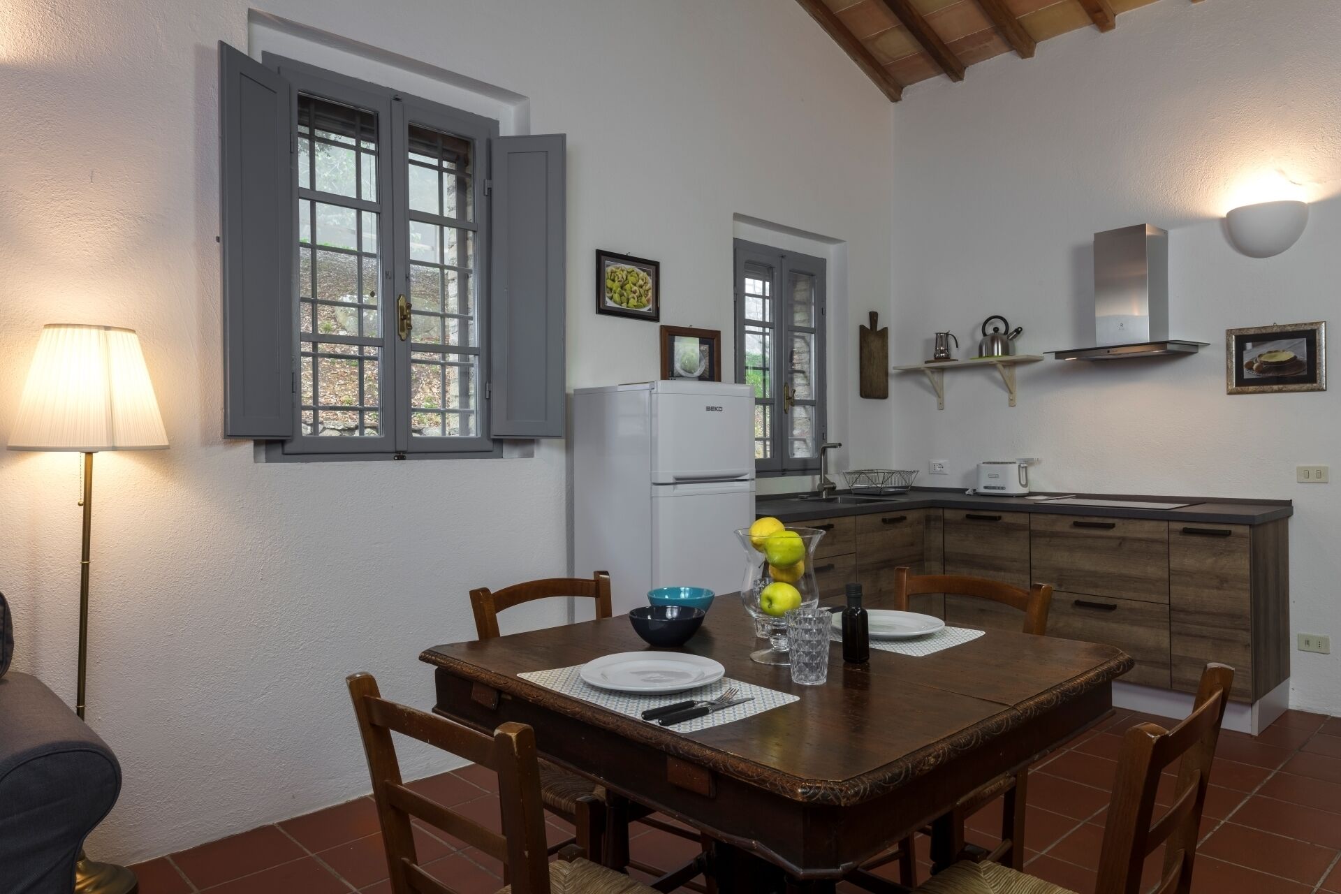 A dining area with a wooden table and chairs, a refrigerator, a sink, and a window with shutters.
