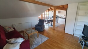 A living room with a red sofa, a glass coffee table, and a TV on a stand. - Sunny top-floor apartment with panoramic balcony & mountain views (Greiling)