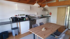 A modern kitchen with a wooden table, chairs, a refrigerator, and a sink. - Sunny top-floor apartment with panoramic balcony & mountain views (Greiling)
