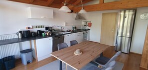 A modern kitchen with a wooden table, chairs, a refrigerator, and a sink. - Sunny top-floor apartment with panoramic balcony & mountain views (Greiling)