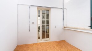 Une petite pièce fermée, dotée d’un sol carrelé, d’une porte avec des panneaux de verre et d’un mur blanc percé d’une fenêtre.