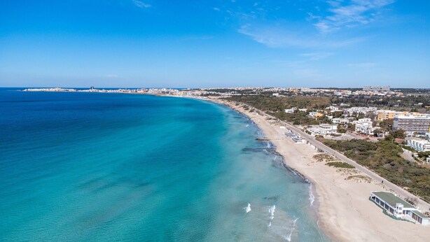 Une vue aérienne d’une zone côtière avec une plage, des bâtiments et un ciel dégagé.