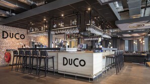 A bar area with a brick wall, bar stools, and shelves of bottles and glasses. - Modern Retreat with Free EV Charging, and On-Site Restaurant Near Autotron (Oss)