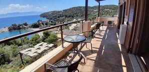 Ein Balkon mit Tisch und Stühlen, der auf eine Küstenlandschaft mit Blick auf das Meer und die Hügel blickt.