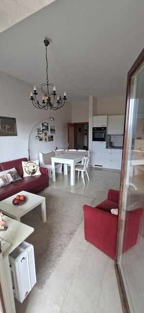 A modern living room with a red sofa, a dining table, and a kitchen area with white cabinets.