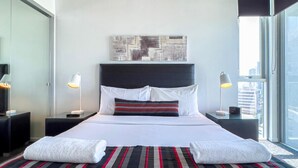Moderni hotellihuone, jossa on suuri sänky, näkymä kaupunkiin ja pelkistetty sisustus.