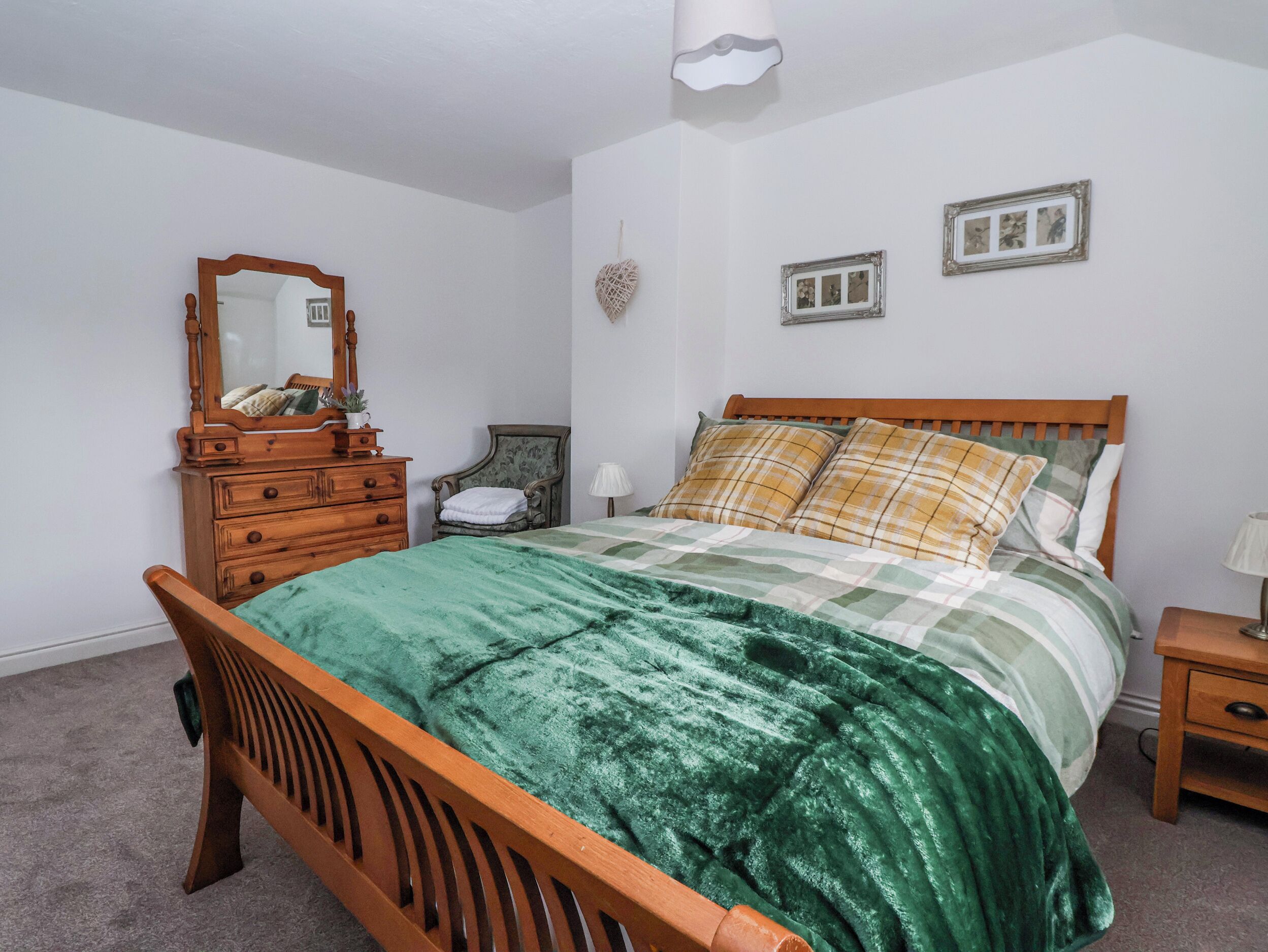 A bedroom with a wooden bed, a dresser, a mirror, and a wall-mounted light fixture.