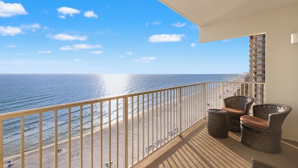 A balcony with wicker furniture, a view of the beach, and a building in the background. - Looking for a Shore Thing? Here it is! 2BR 2.5ba Sleeps 8! Beachfront! (Panama City Beach)