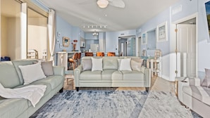 A spacious living room with a light-colored sofa, a coffee table, and a ceiling fan. - Looking for a Shore Thing? Here it is! 2BR 2.5ba Sleeps 8! Beachfront! (Panama City Beach)