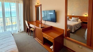 Ett hotellrum med en säng, ett skrivbord, en tv och en stor spegel.