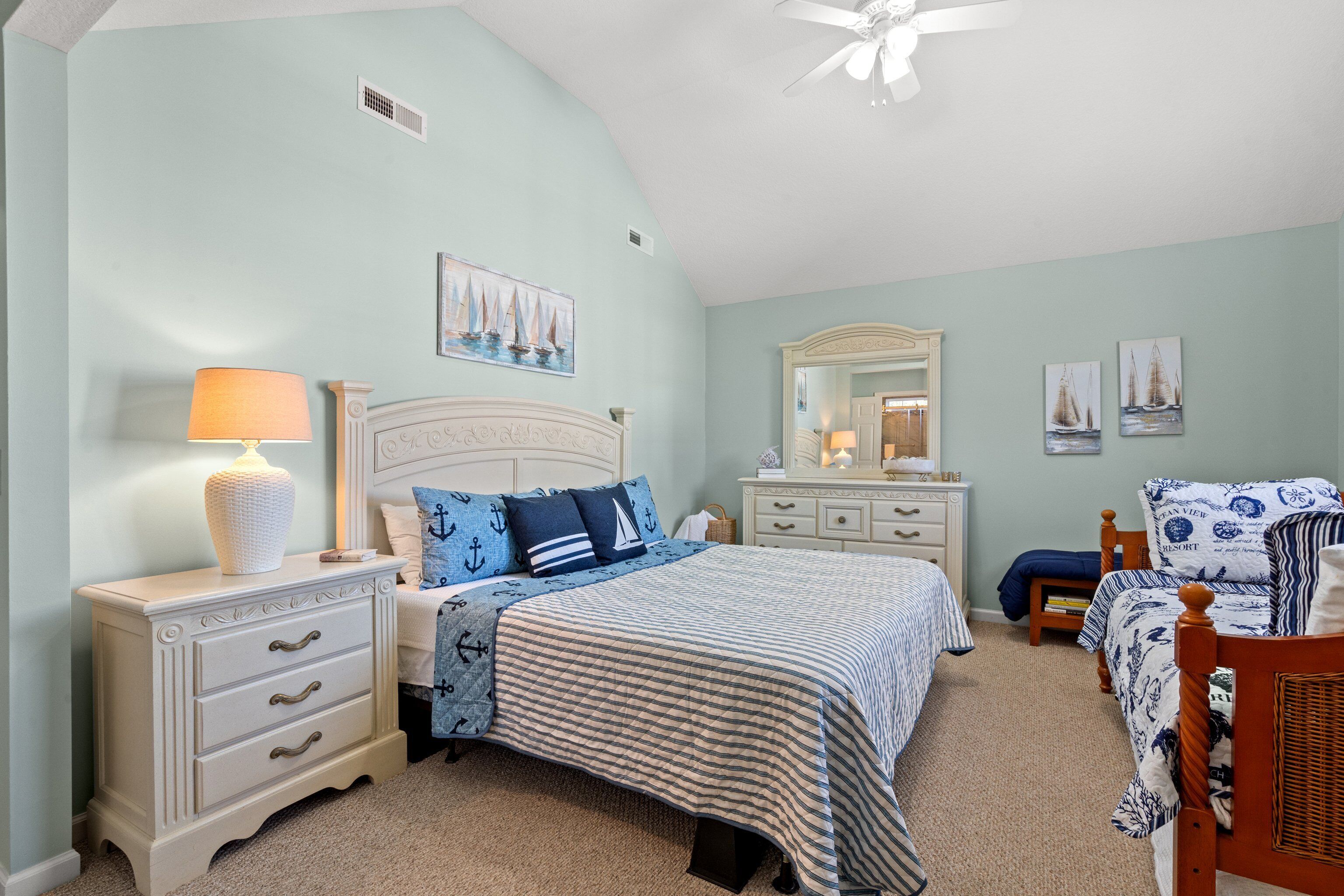 Une chambre à coucher comprenant un lit, une table de chevet, une commode, un miroir et un ventilateur de plafond.