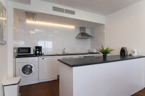 A modern kitchen with a dishwasher, microwave, kettle, and a small island with a plant. - 279 Blau Blue 1 by Mallorca Charme (Can Picafort)