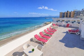 Une terrasse sur le toit, dotée de chaises longues et d’une table, offrant une vue sur une plage et l’océan.