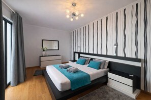 Een moderne slaapkamer met een bed, nachtkastjes, een kaptafel, een spiegel en een opvallend gestreept wandontwerp.