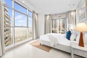 Et moderne hotelværelse med en stor seng, et natbord med lampe og udsigt over byen gennem gulv til loft-vinduer.
