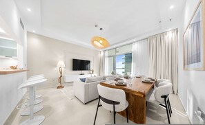 Et moderne spiseområde med et træbord, hvide stole og et fjernsyn i baggrunden.
