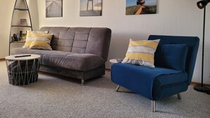 A living room with a grey sofa, a blue armchair, and a small round table. There are three framed pictures on the wall. - Holiday Apartment Zwischenwasser (Jübek)
