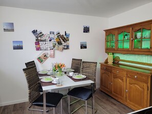 Ein Essbereich mit einem Tisch für vier Personen, umgeben von Korbstühlen, einer Holzkabine mit Glastüren und an der Wand befestigten Fotografien.