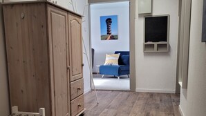 A room with a wooden wardrobe, a blue sofa, a small chalkboard, and a framed picture on the wall. - Holiday Apartment Zwischenwasser (Jübek)
