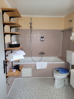Ein Badezimmer mit Badewanne, Toilette, Regalen mit Handtüchern und einer Dusche.