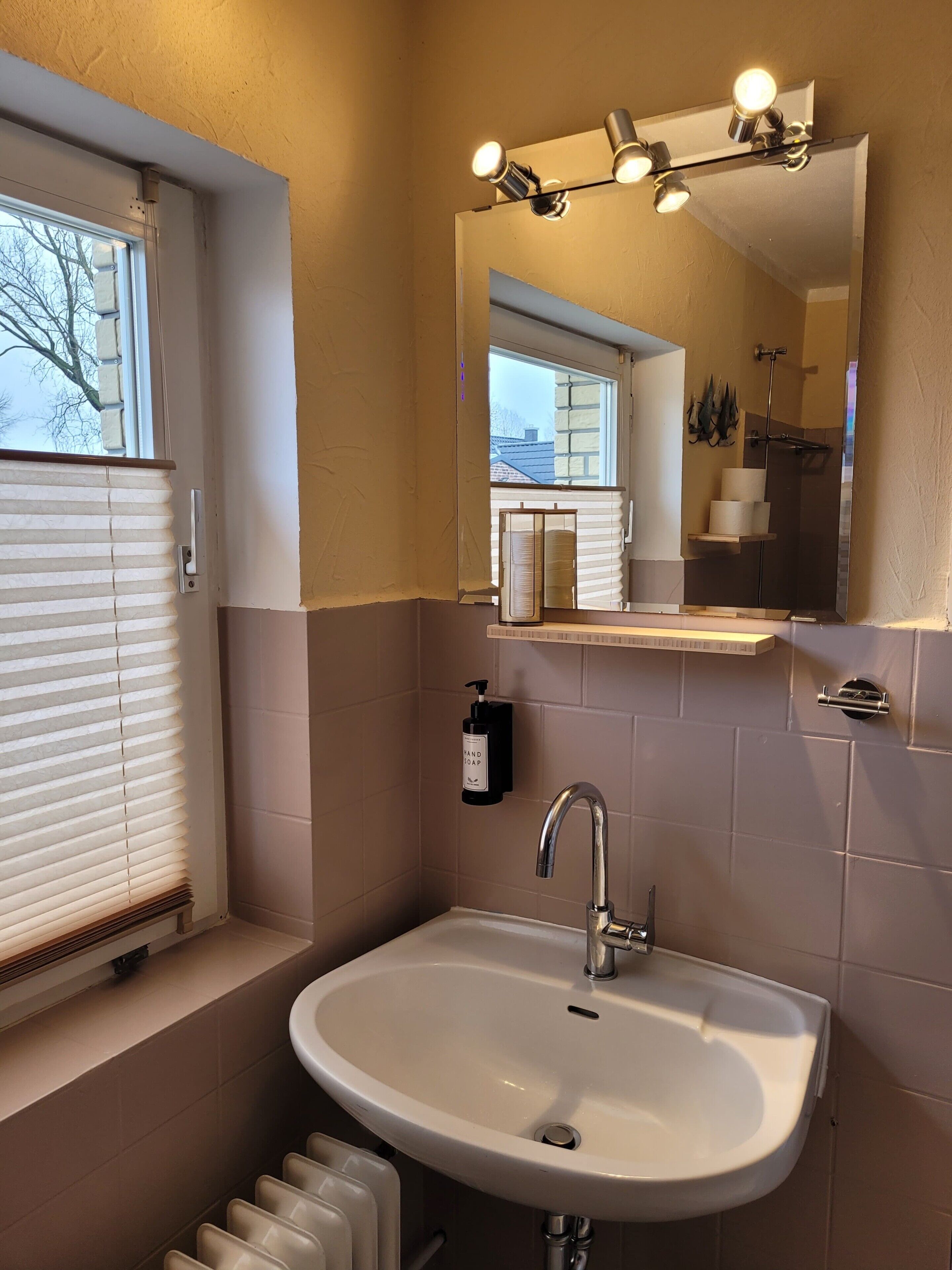 Une salle de bain avec un lavabo, un miroir et une fenêtre équipée de stores.